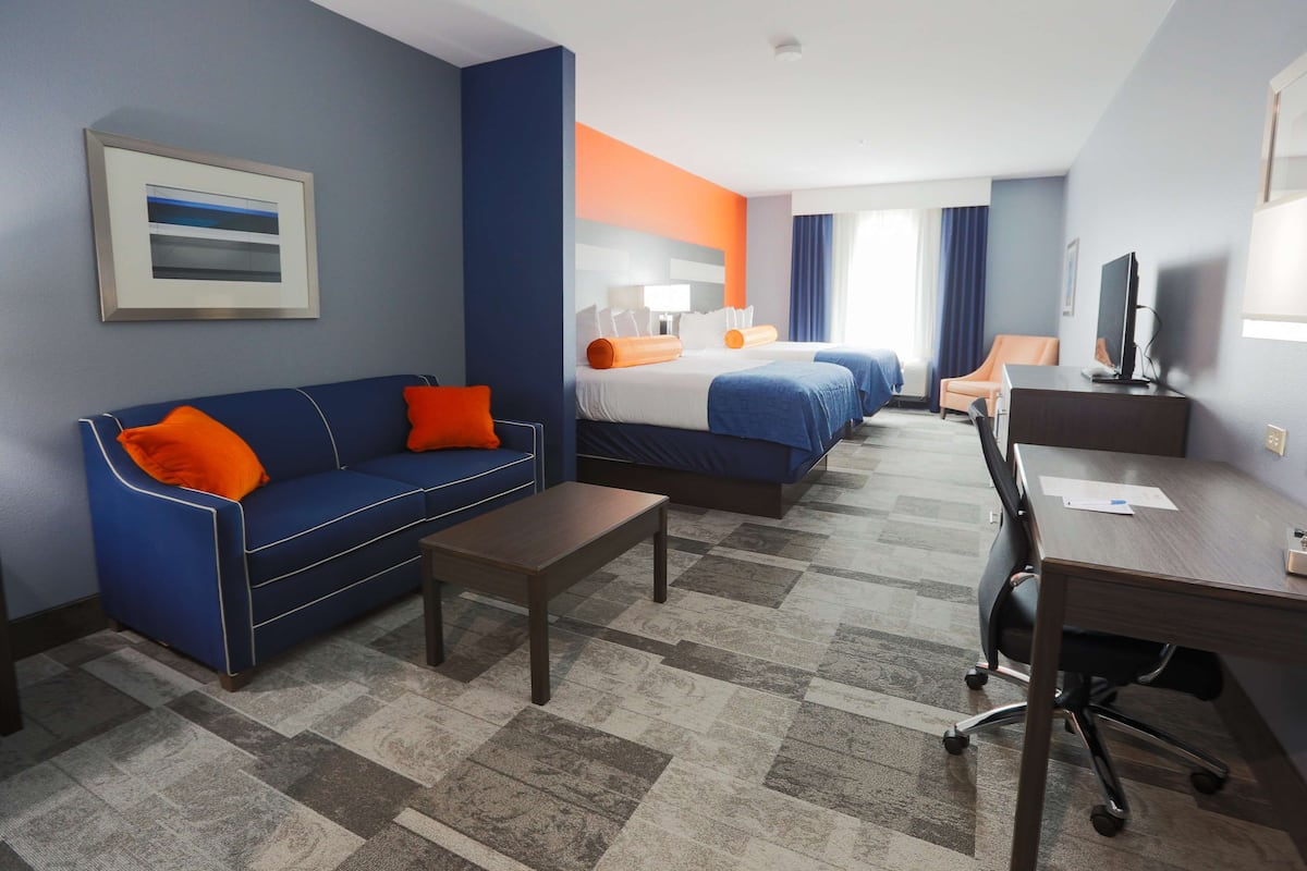 A hotel room with a blue sofa, a bed with orange pillows, a desk, and a television.