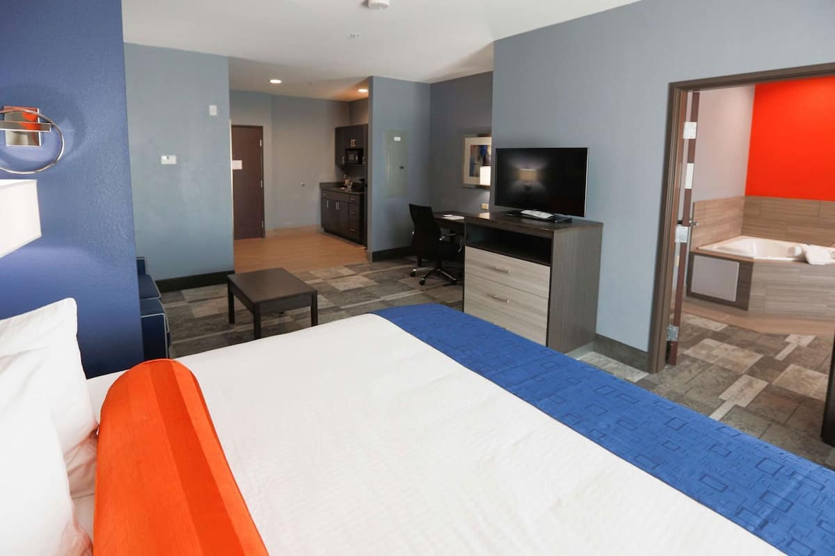 A hotel room with a bed, desk, television, and a bathroom with a bathtub.