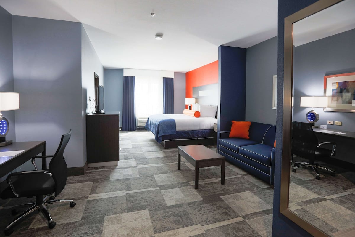 A hotel room with a bed, a desk with a chair, a sofa, and a small table.