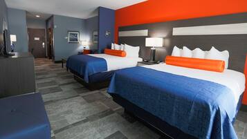 A hotel room with two beds, each with blue bedding and orange headboards, a desk, and a chair.