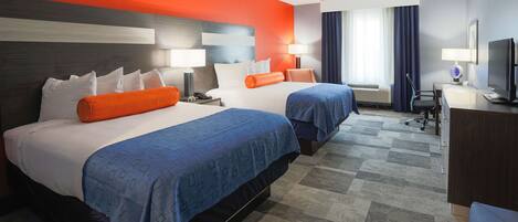 A hotel room with two beds, a desk, a television, and a window with curtains.
