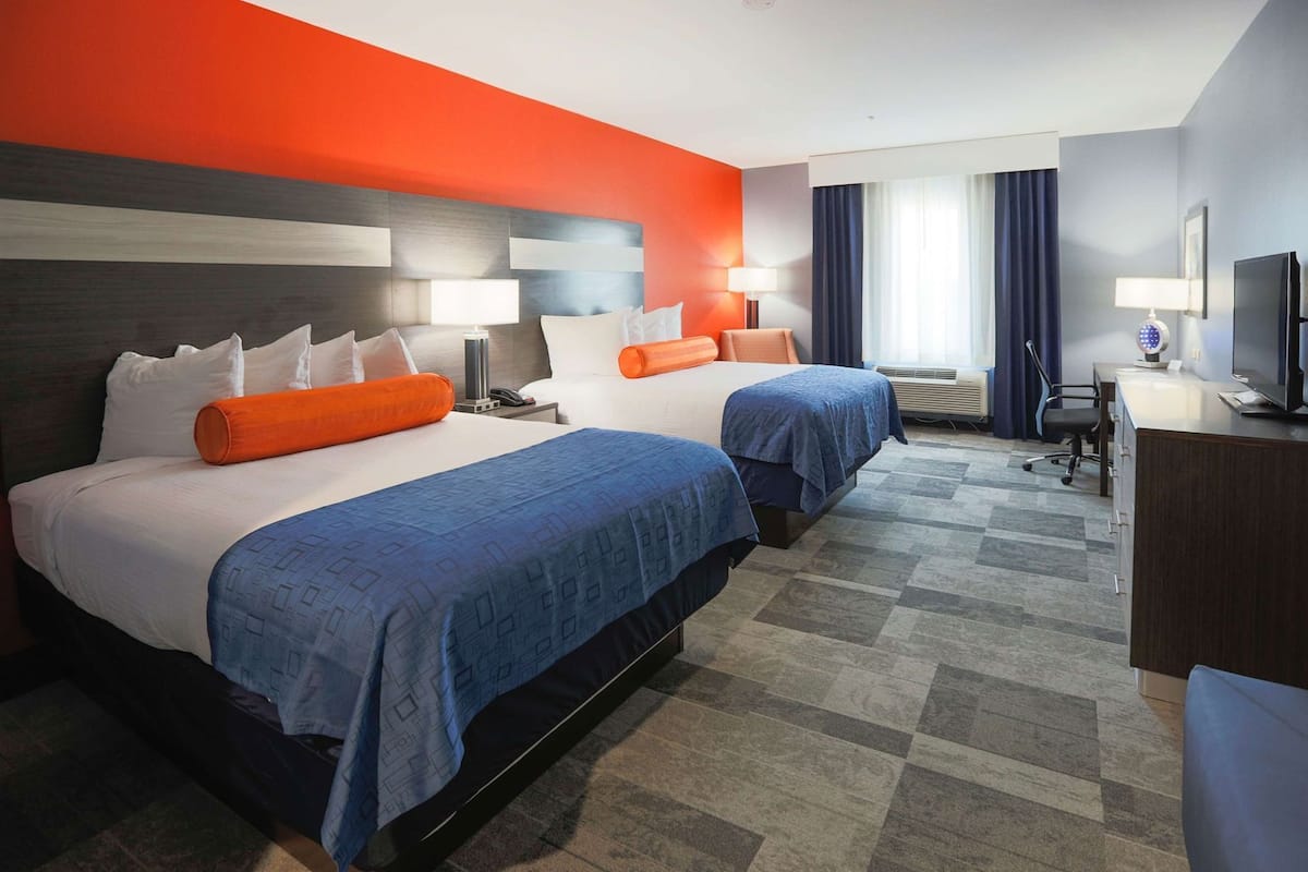 A hotel room with two beds, a desk, a TV, and a window with curtains.