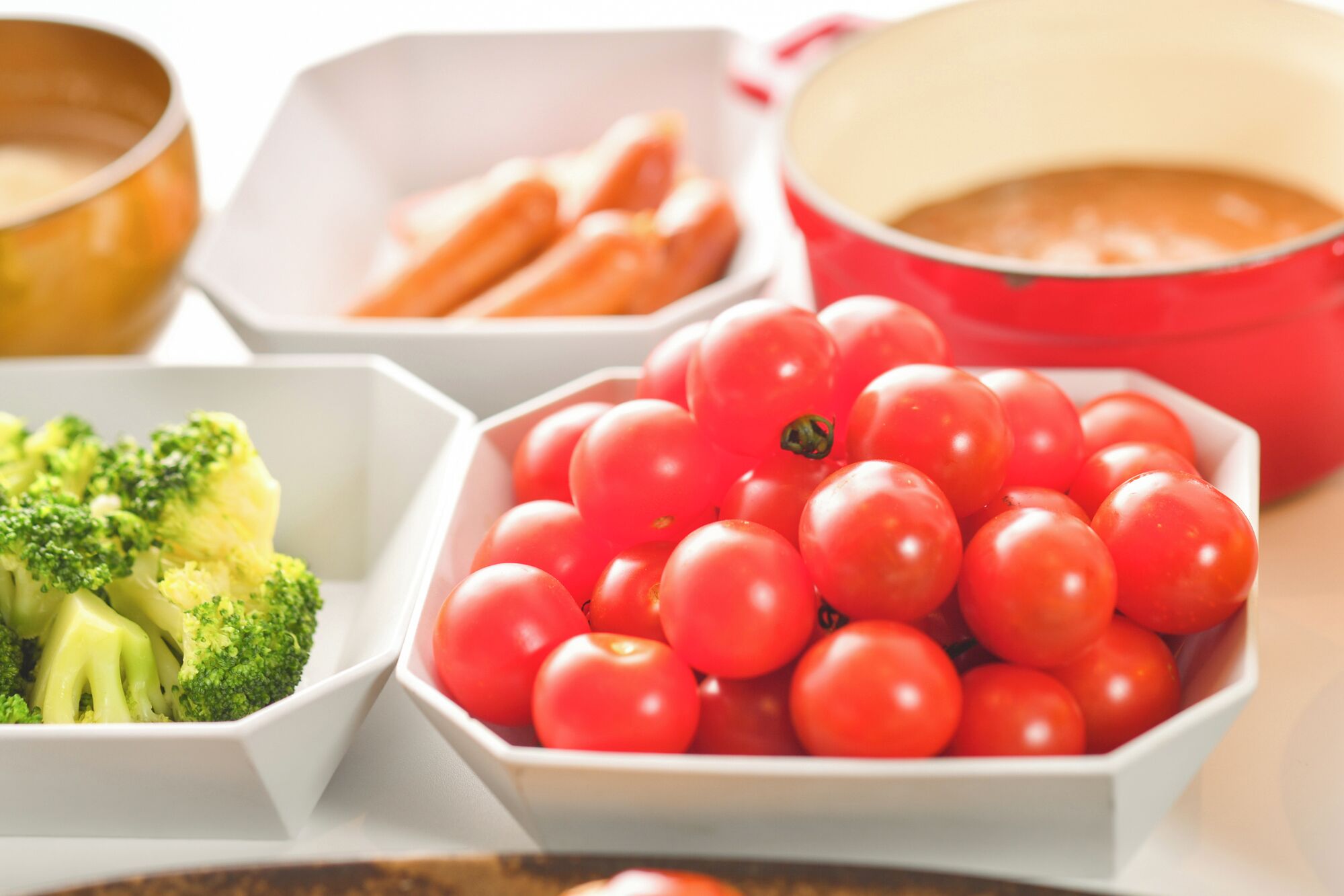 A variety of food items including broccoli, cherry tomatoes, and carrots in white bowls.