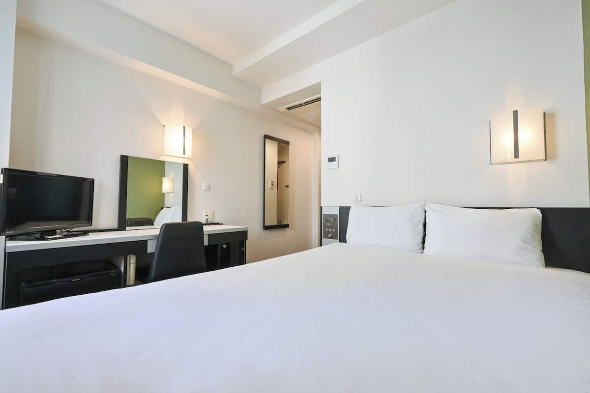 A hotel room with a bed, a desk with a computer, a chair, and a TV.
