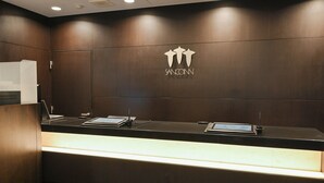 Un mostrador de recepción con acabado de madera oscura, un logotipo en la parte superior y dos computadoras portátiles sobre la barra.