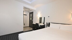Habitación de hotel con una cama grande, un escritorio con silla, un espejo y una puerta que da a otra habitación.