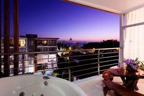 A balcony with a hot tub, a wooden table with flowers, and a view of buildings and a sunset. - At Sea Condo (Krabi)