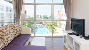 Una sala de estar moderna con un amplio ventanal, un sofá, un televisor y vista a la piscina.