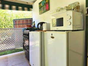 A kitchen with a stove, oven, microwave, and refrigerator. There is a wooden fence and a window with a view of greenery. - Te Ava Piti Lodge (Raiatea)