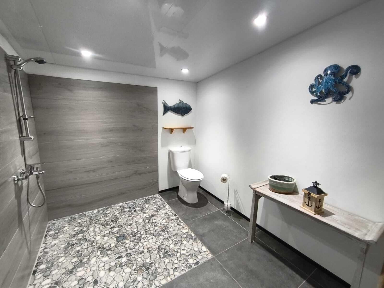 Een badkamer met douche, toilet en decoratieve muurkunst in de vorm van vissen.
