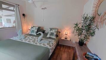Un dormitorio con cama, mesita de noche, lámpara, planta en maceta y un adorno en la pared.