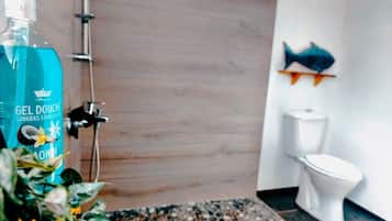 A bathroom with a shower, a toilet, and a bottle of gel on the floor.