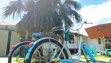 Uma bicicleta estacionada sob uma palmeira em área externa com uma mesa e cadeiras.