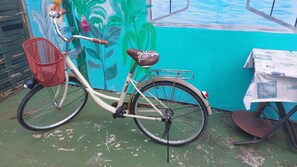 A bicycle with a basket and a seat with a decorative pattern, parked against a wall with a mural. - Te Ava Piti Lodge (Raiatea)