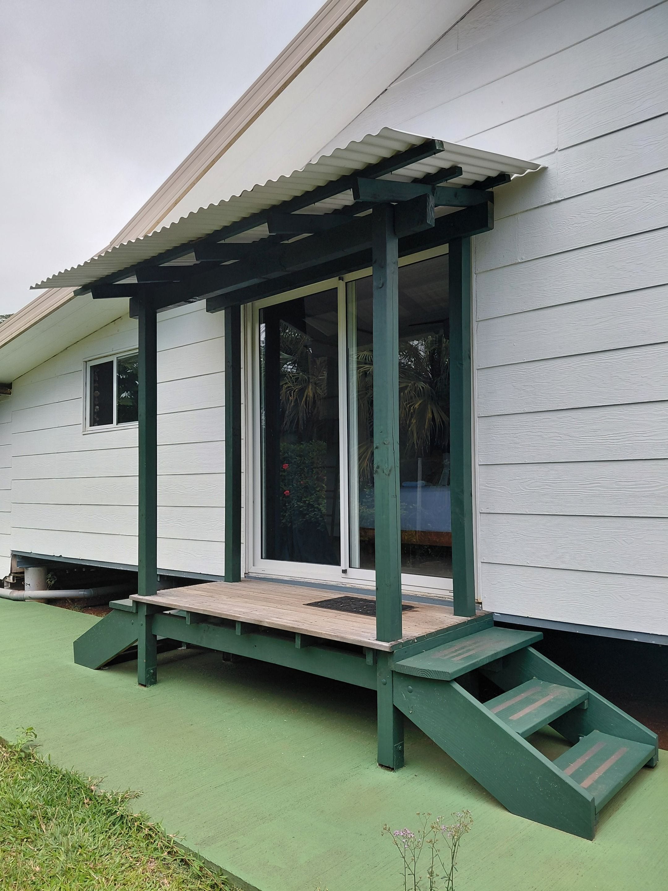 A house with a covered porch, a green ramp, and a window with a view of palm trees.