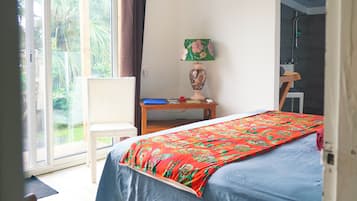 A room with a bed, a chair, a table, a lamp, and a view of greenery outside.
