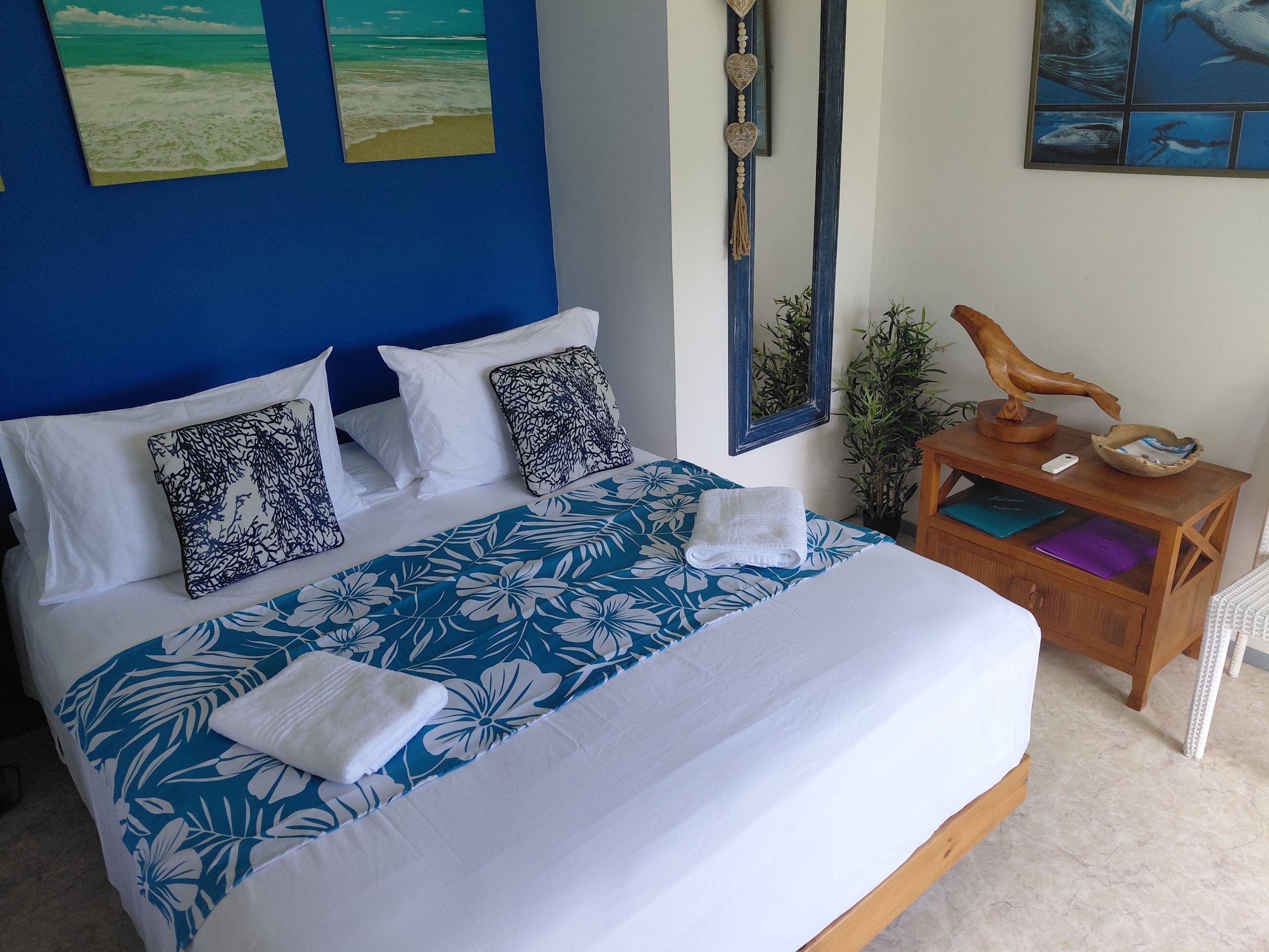 A neatly made bed with floral bedding, a wooden nightstand with a lamp, and a framed mirror on the wall.