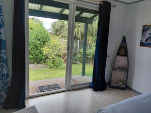 A room with a sliding glass door leading to a balcony, a surfboard, and a welcome mat. - Te Ava Piti Lodge (Raiatea)