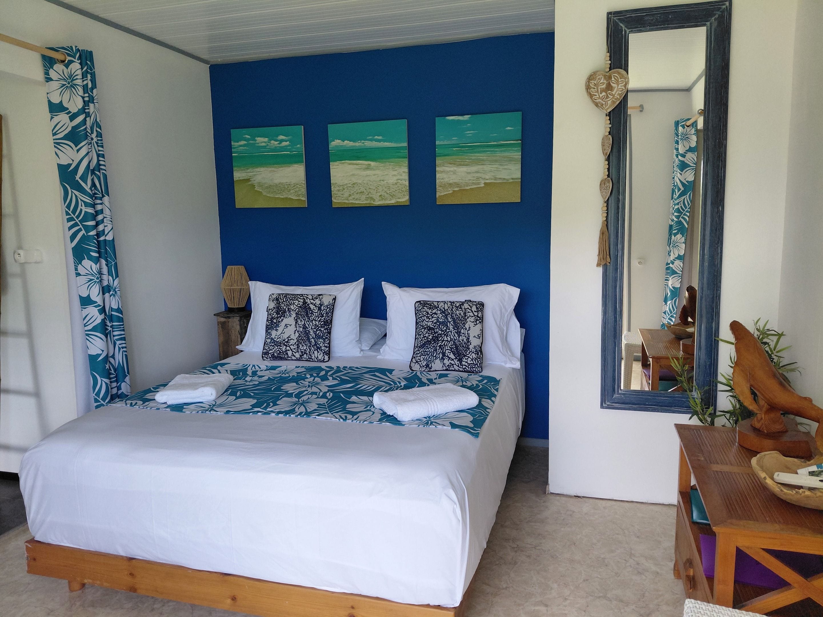 Quarto com cama, mesa de cabeceira, espelho e uma parede com três quadros.