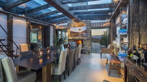 A cozy outdoor dining area with a stone fireplace, wooden beams, and a view of the landscape. - Mahu Whenua (Treble Cone)