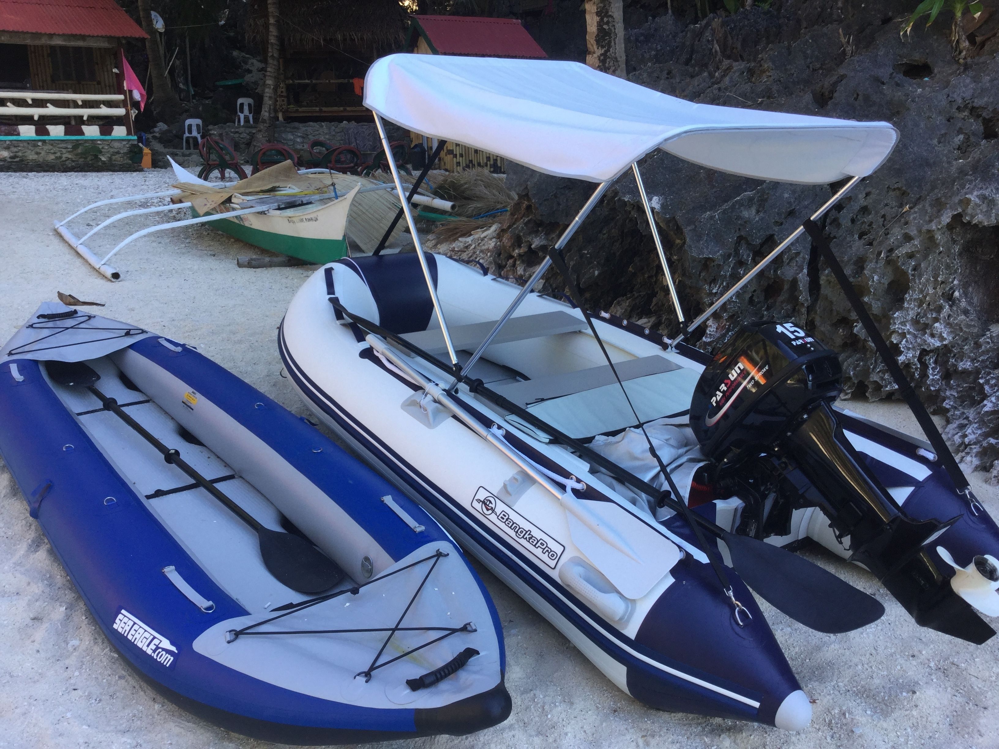 Dos botes inflables con barandillas laterales y un motor, una tabla de paddleboard y una pequeña cabaña al fondo.