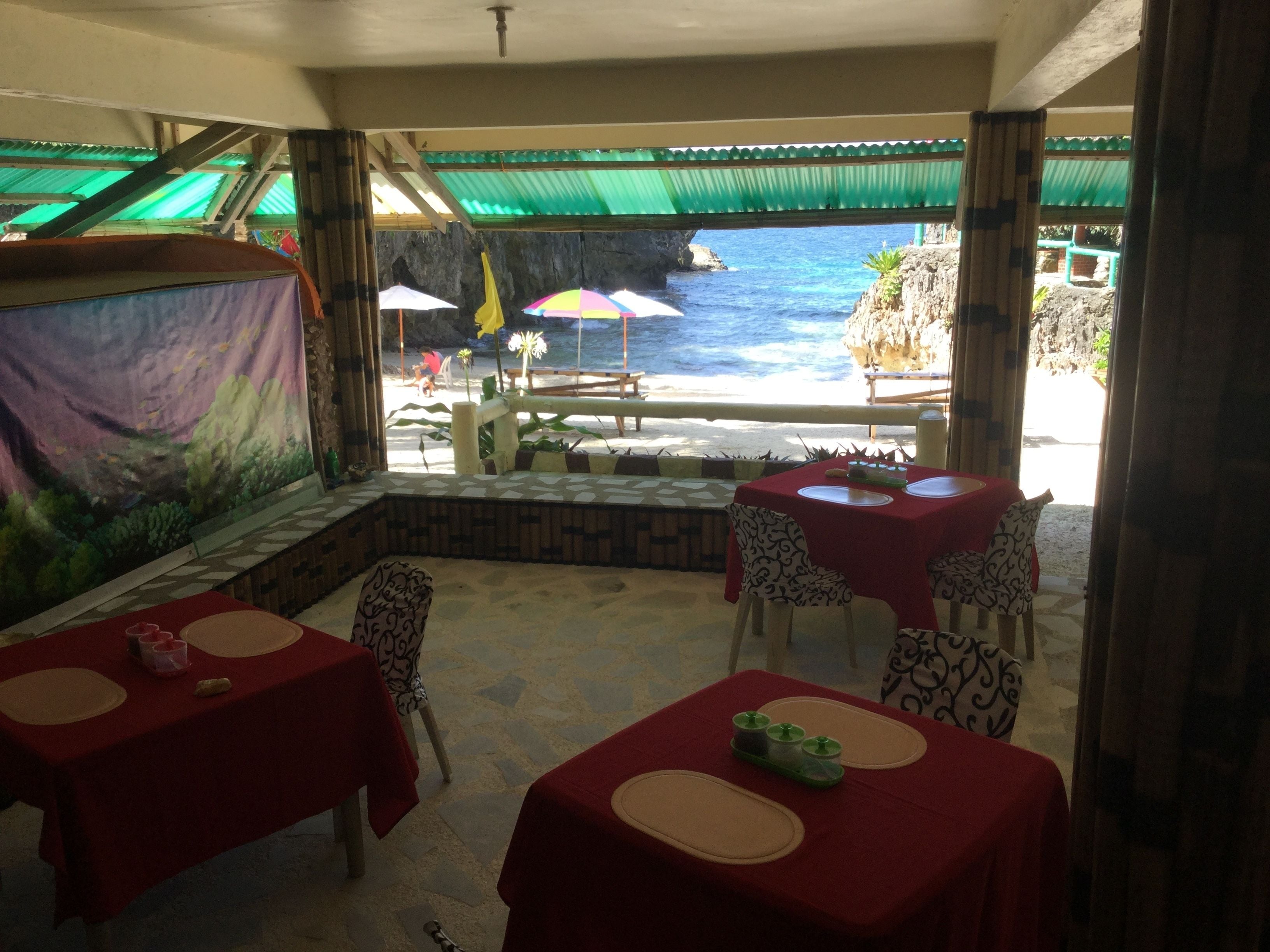 Un restaurant doté d’une terrasse offrant une vue sur la mer, avec des tables recouvertes de nappes rouges et des chaises à motifs.