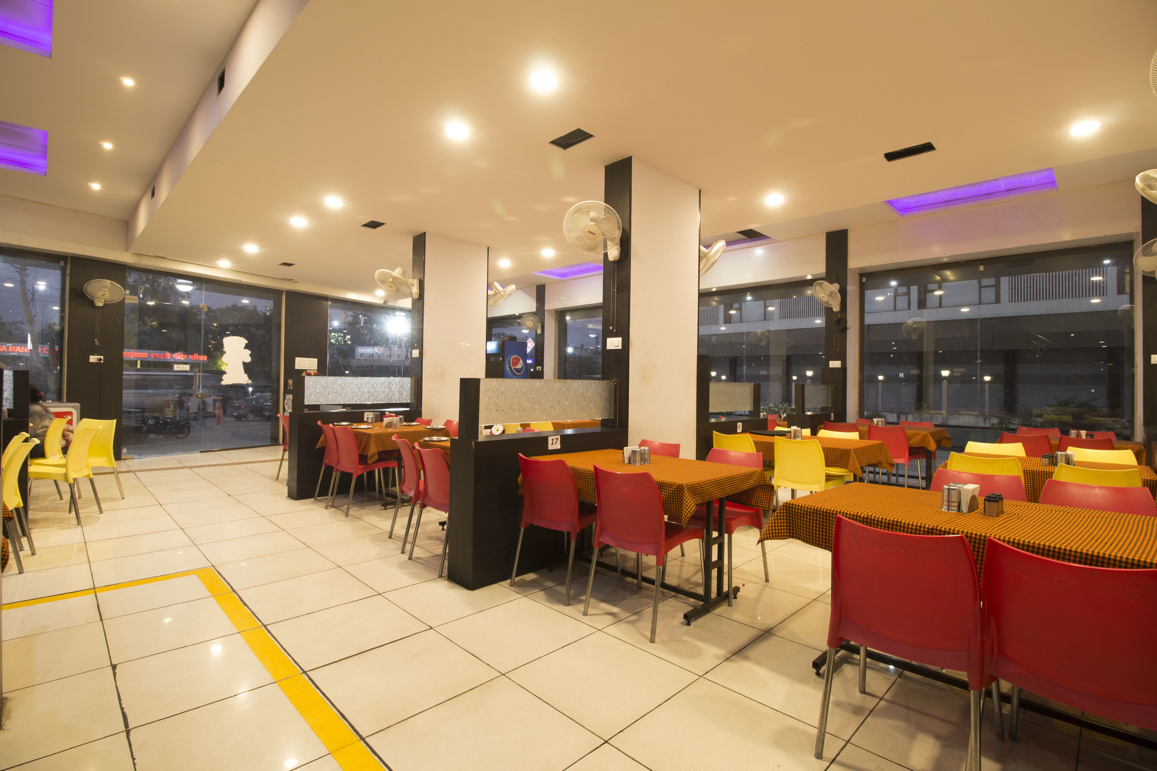 Un restaurante con varias mesas y sillas, ventanas amplias e iluminación en el techo.