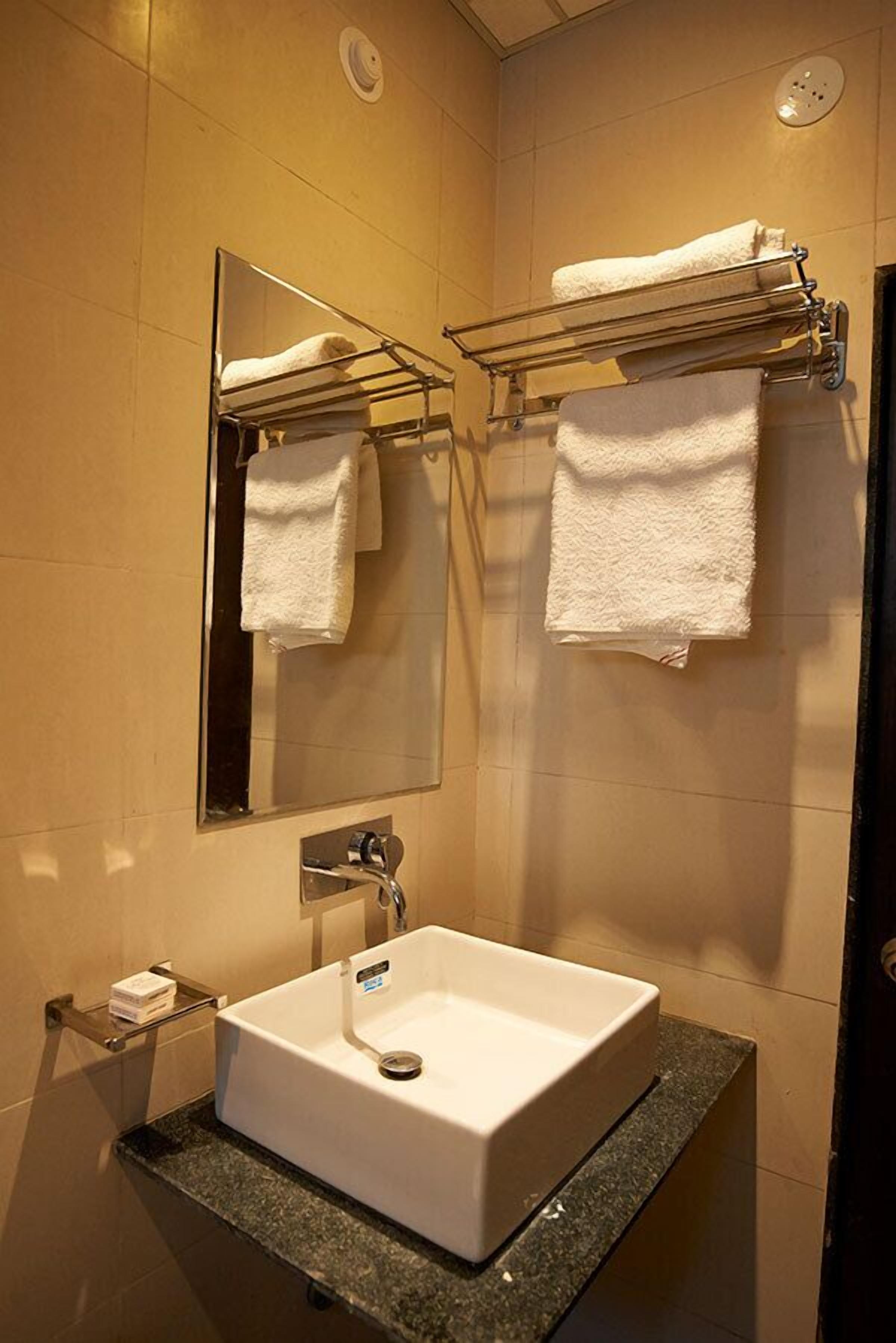A bathroom with a white sink, a mirror, and two towel racks with white towels.