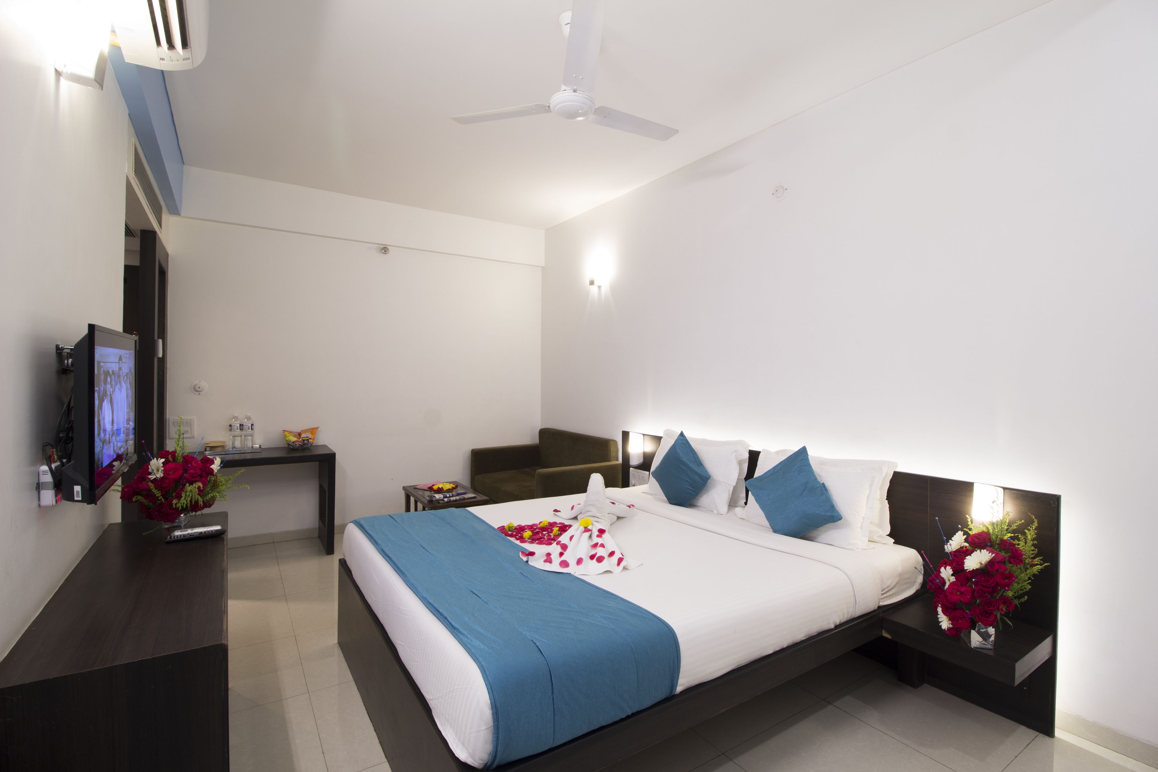 A modern hotel room with a bed, bedside tables, a desk, a TV, and a ceiling fan.