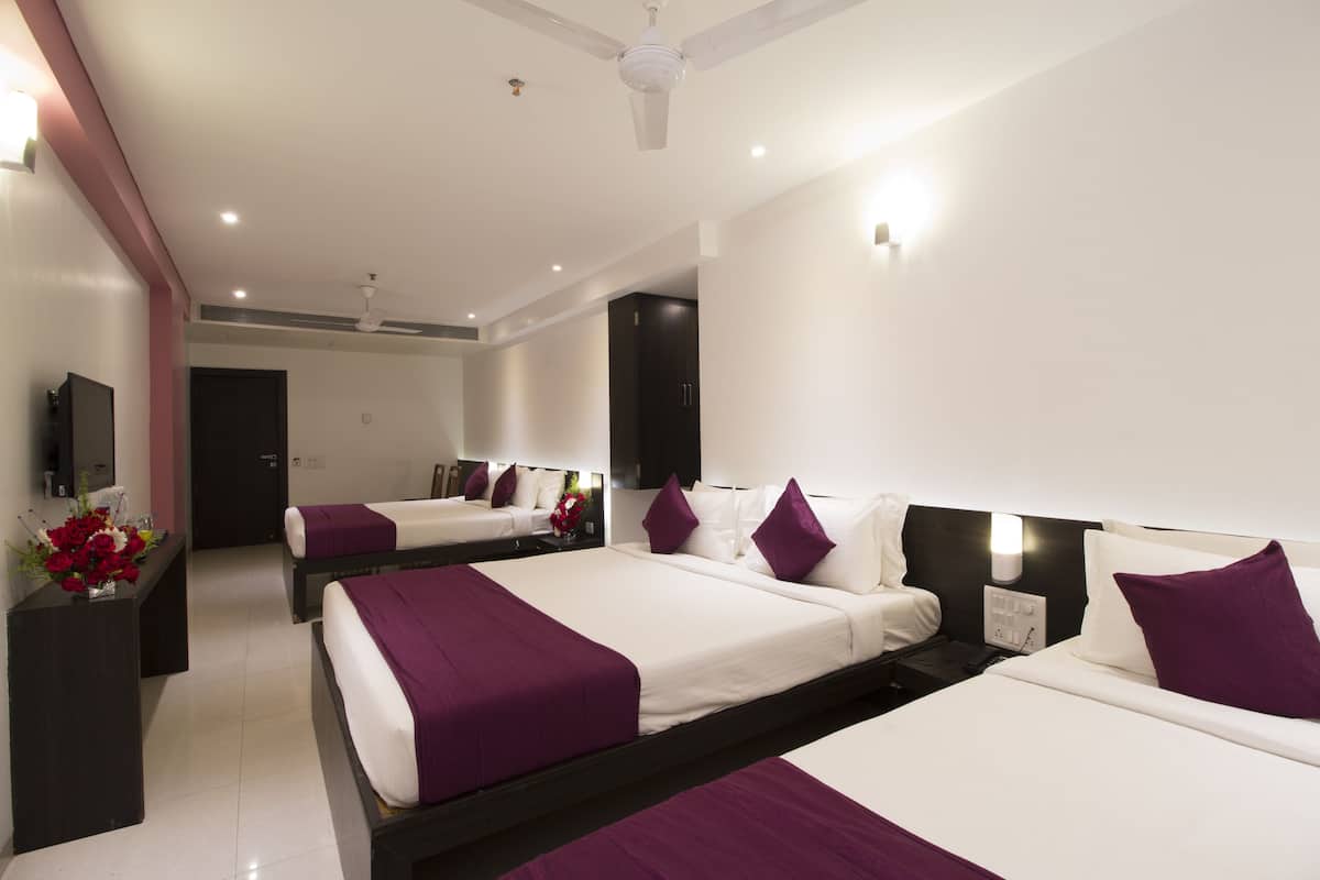 A hotel room with three beds, a ceiling fan, and a TV on the wall.
