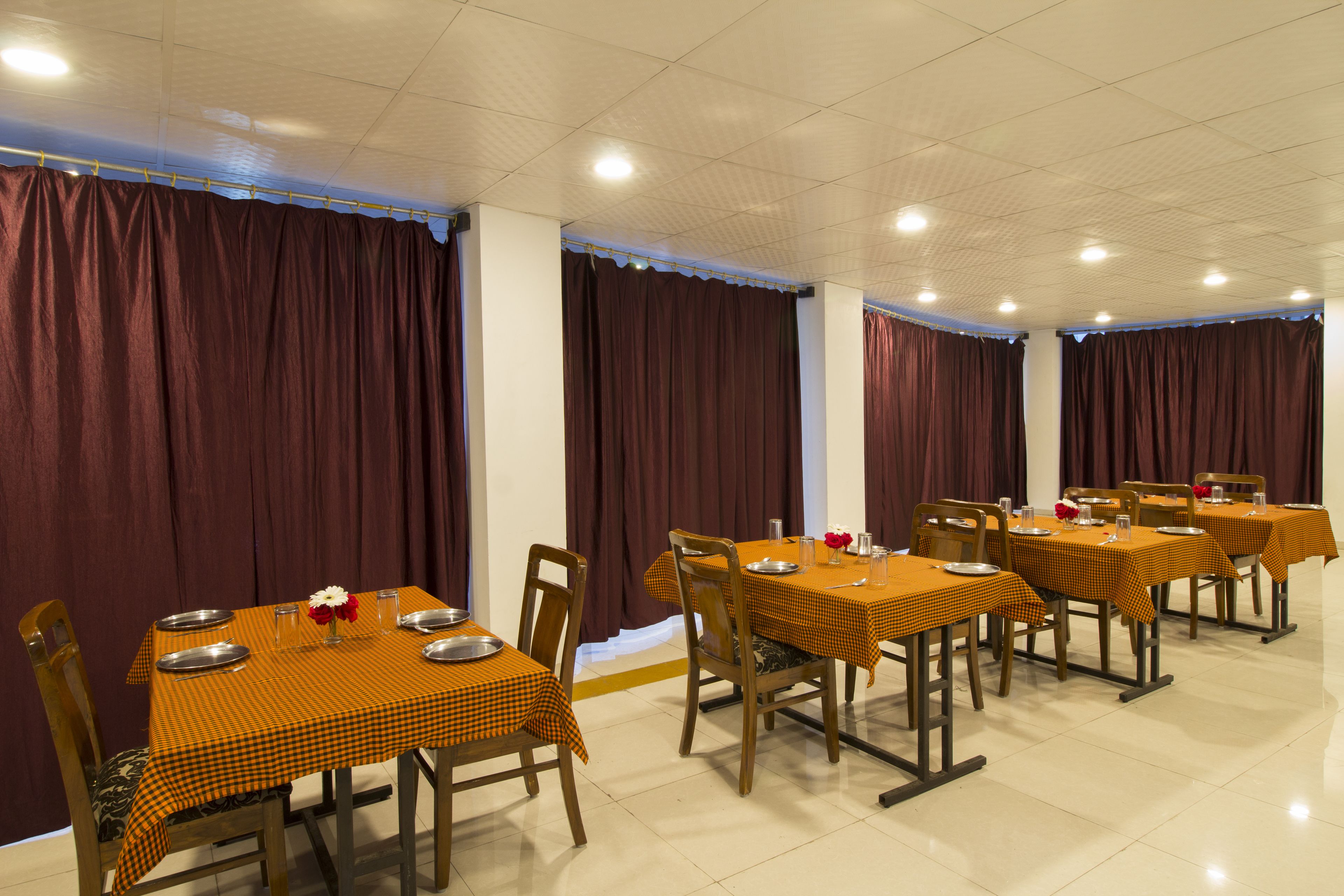 A dining area with multiple tables set for service, each with a checkered tablecloth and metal serving trays.
