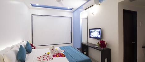 A modern hotel room with a bed, a flat-screen TV, a desk, and a mirror.