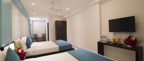 A hotel room with two beds, a TV, a desk with a vase of flowers, and a ceiling fan.