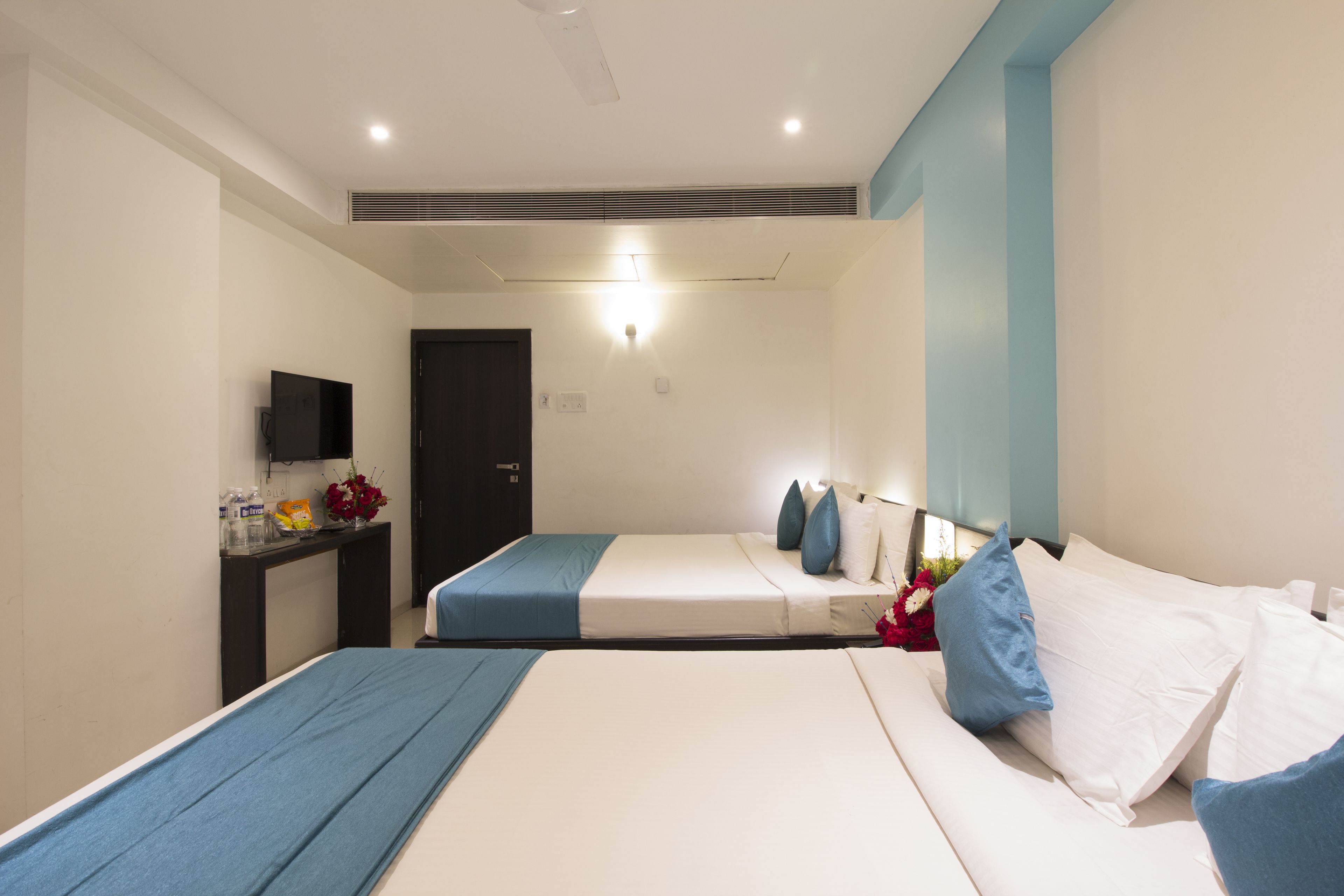 A hotel room with two beds, a desk, a TV, and a door.