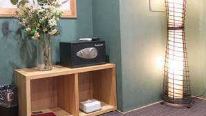 Ein Zimmer mit einem Holzkasten, einer Vase mit Blumen, einer Lampe und einem Fenster mit Gittermuster.