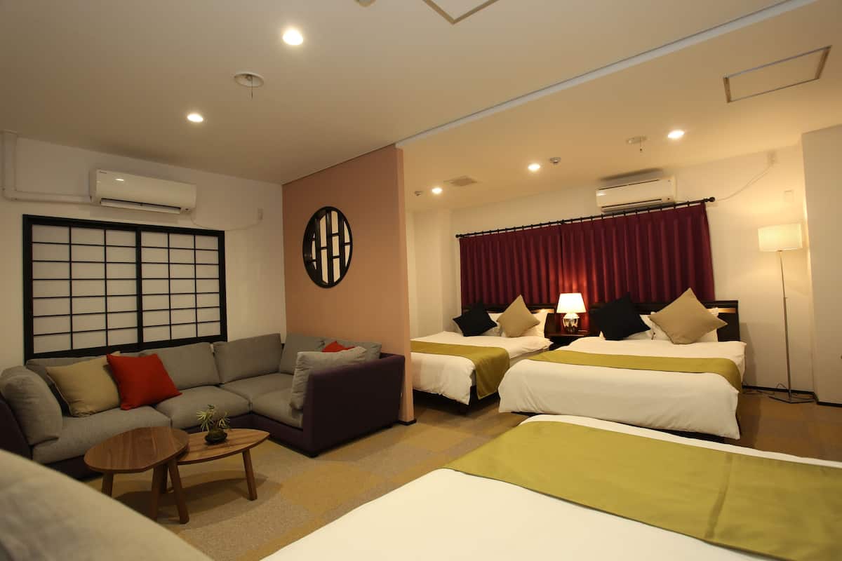 A hotel room with a sofa, two single beds, a small table, and a lamp.
