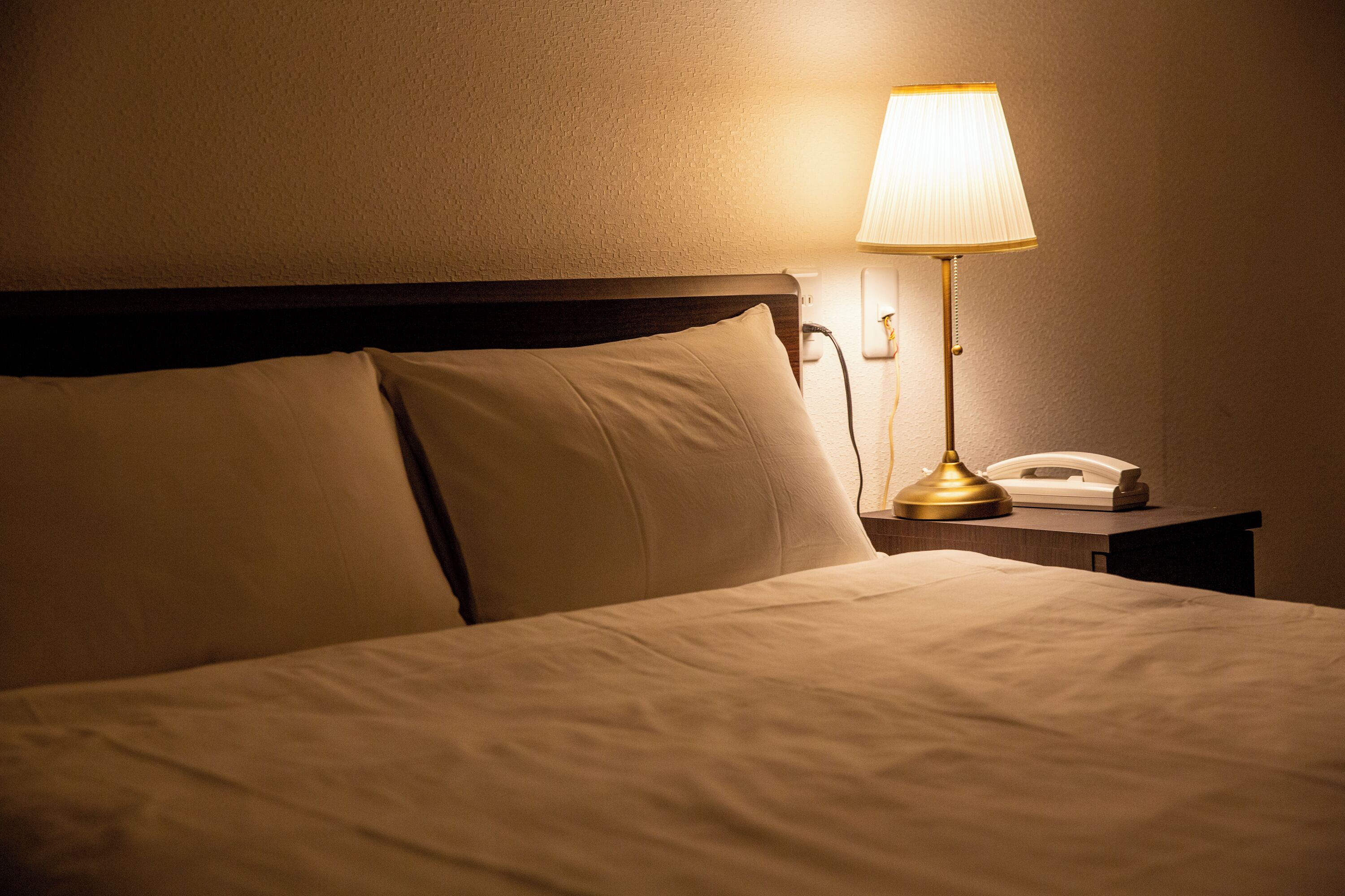 A neatly made bed with a headboard, a bedside lamp, and a telephone on a nightstand.