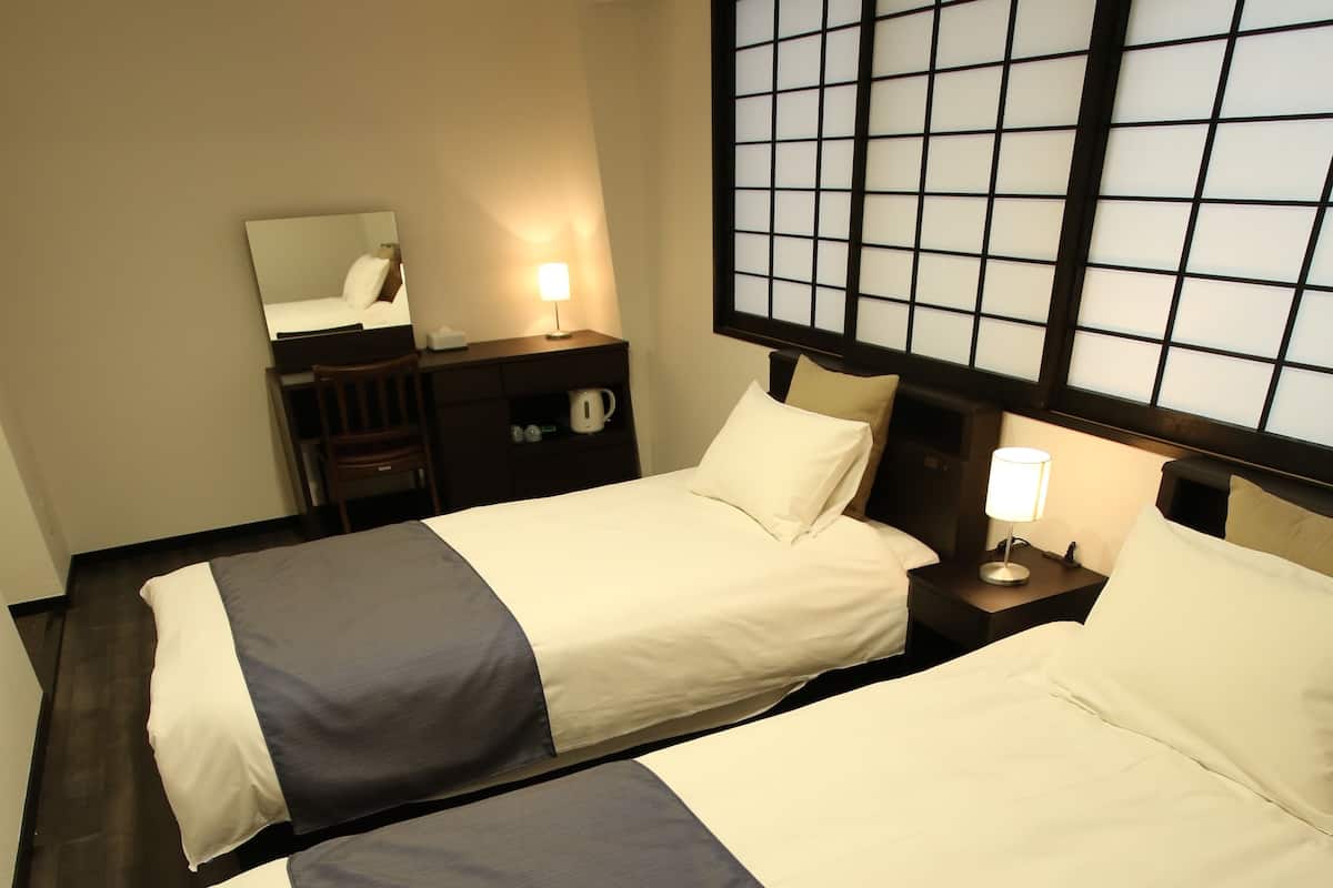 A hotel room with two beds, a nightstand with a lamp, a mirror, and a dark wooden floor.