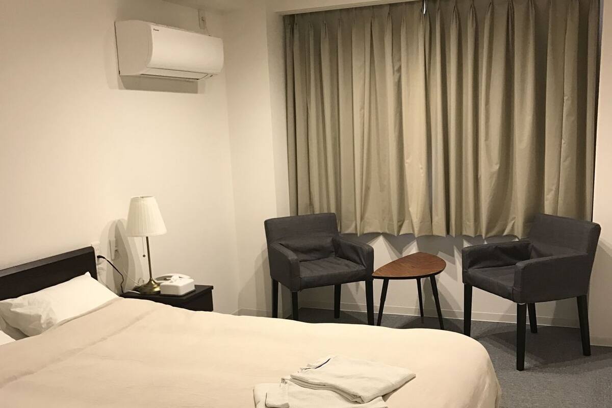 A hotel room with a large bed, two armchairs, a small table, a lamp, and a window with curtains.