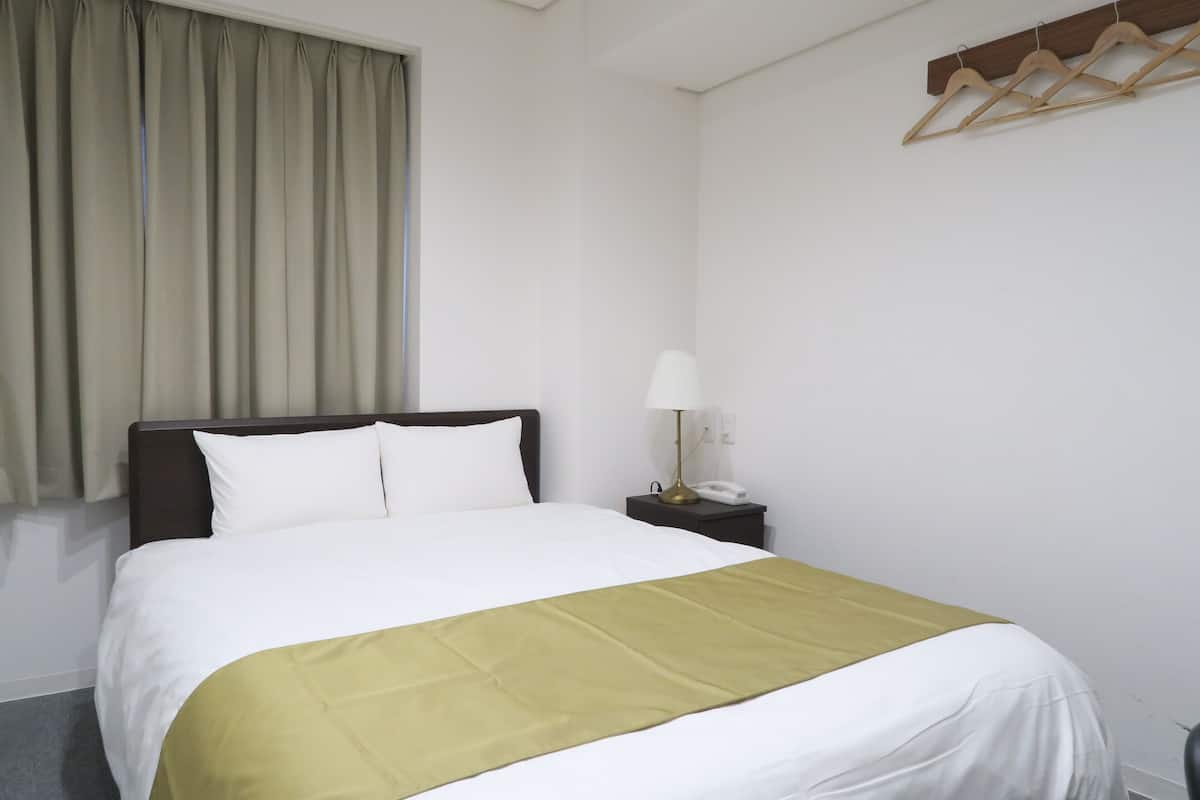 A hotel room with a bed, a nightstand with a lamp, and a wooden hanger rack.