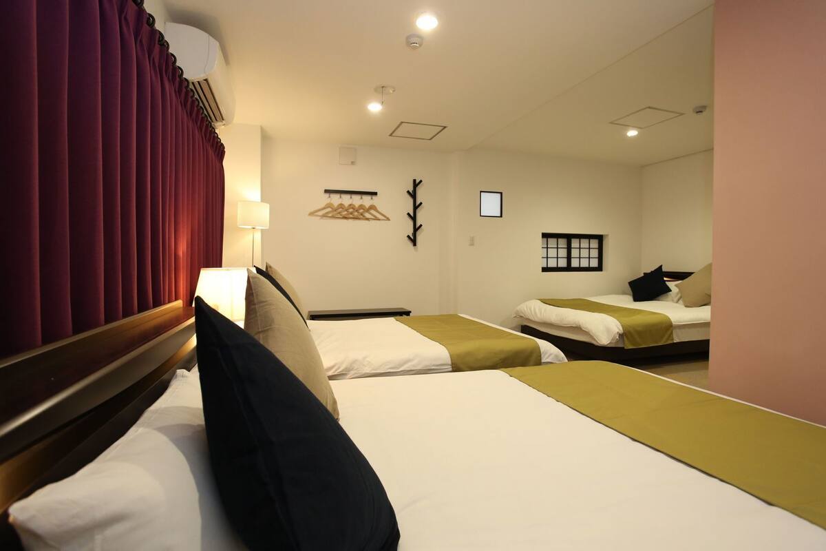 A hotel room with two beds, a mirror, a wall-mounted light, and a small window.