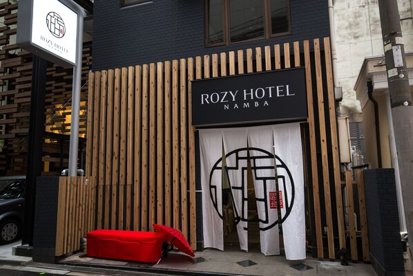 Entrada de un hotel con fachada de madera y un letrero que dice 'ROZY HOTEL NAMBALA'.