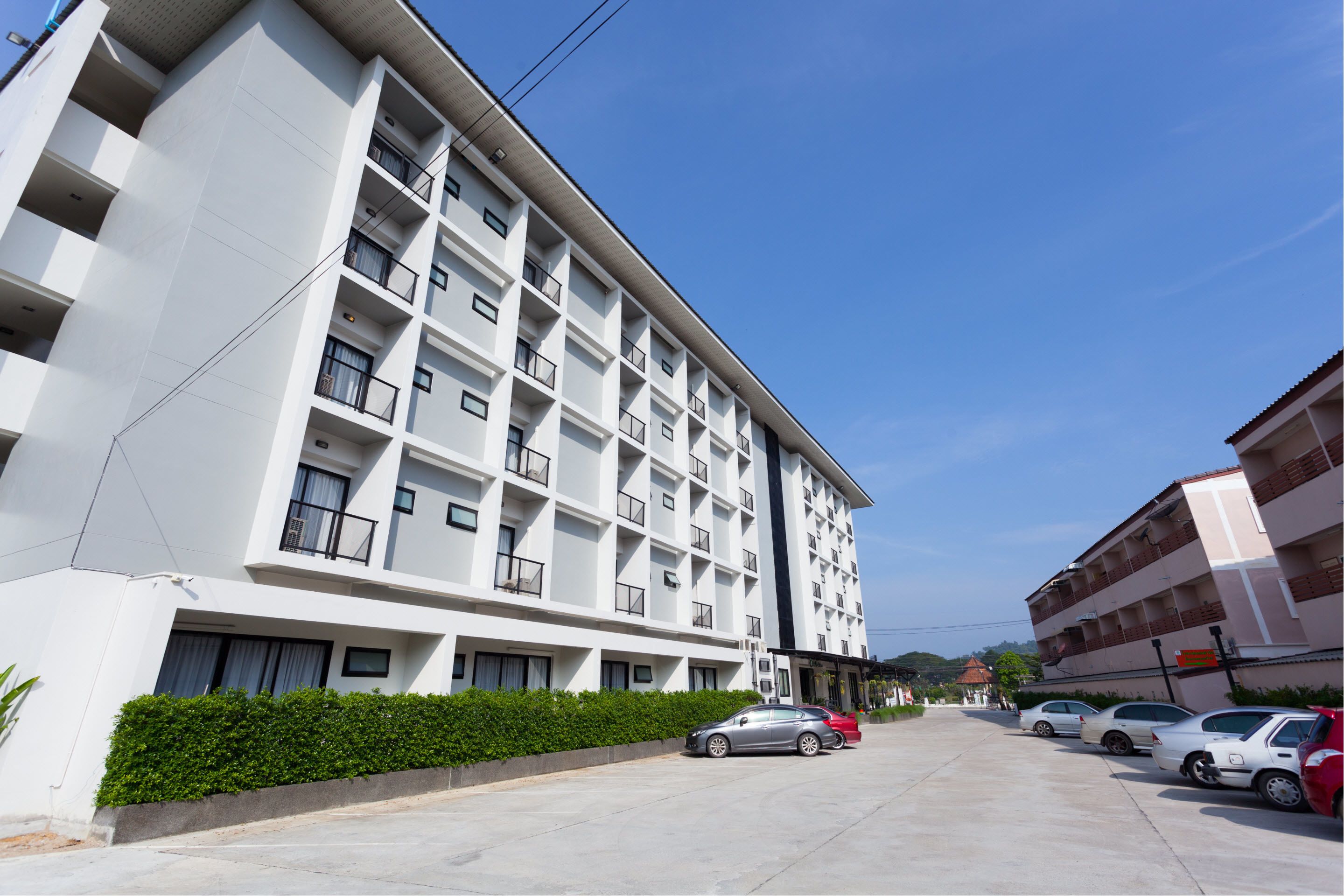 Un hotel de varios pisos con un diseño moderno, que cuenta con balcones en cada planta y un estacionamiento con varios automóviles.