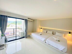 Habitación de hotel con dos camas, un ventanal grande con cortinas, un escritorio con silla y vistas a la ciudad.