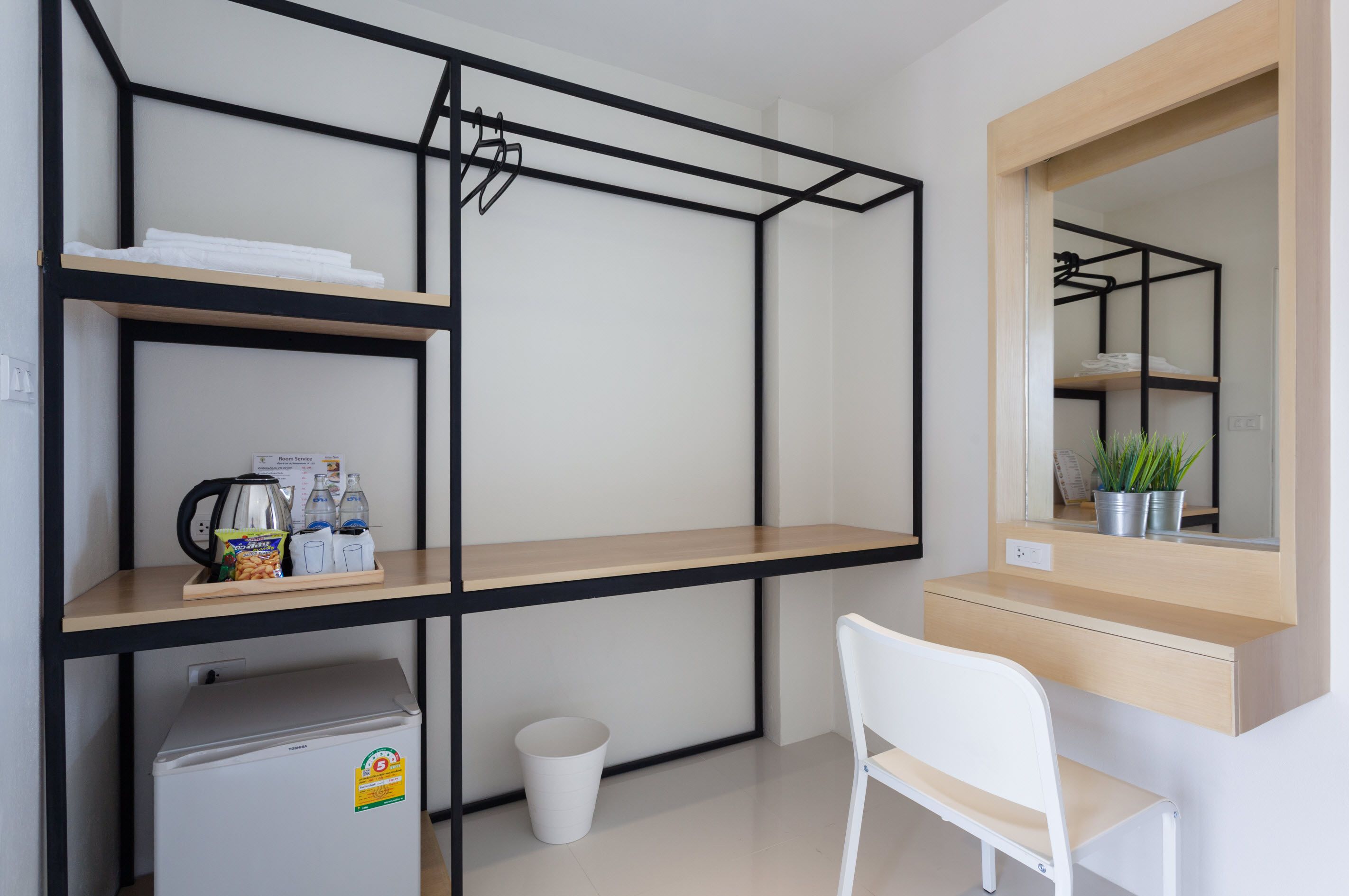 A compact room with a bed, a desk, and a chair. There is a small trash bin and a radiator.