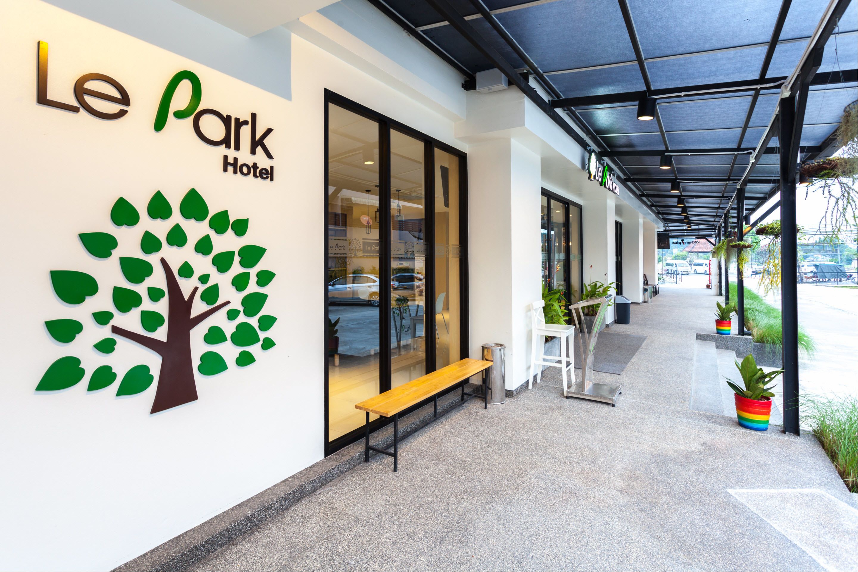 The exterior of Le Park Hotel with a tree logo, a bench, and potted plants along the walkway.