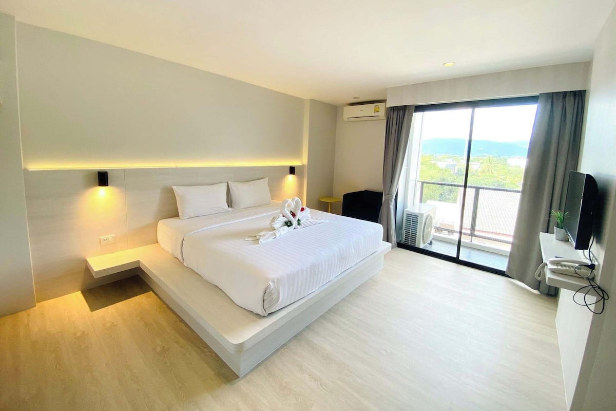 Quarto de hotel moderno com uma cama grande, televisão de tela plana, escrivaninha com telefone e varanda com vista.