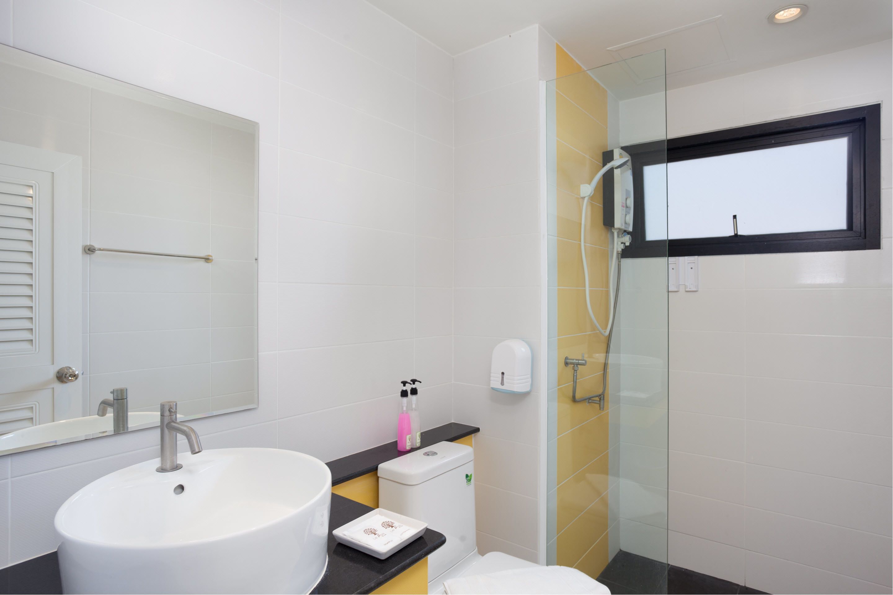 A modern bathroom with a white sink, a glass shower enclosure, and a black countertop.
