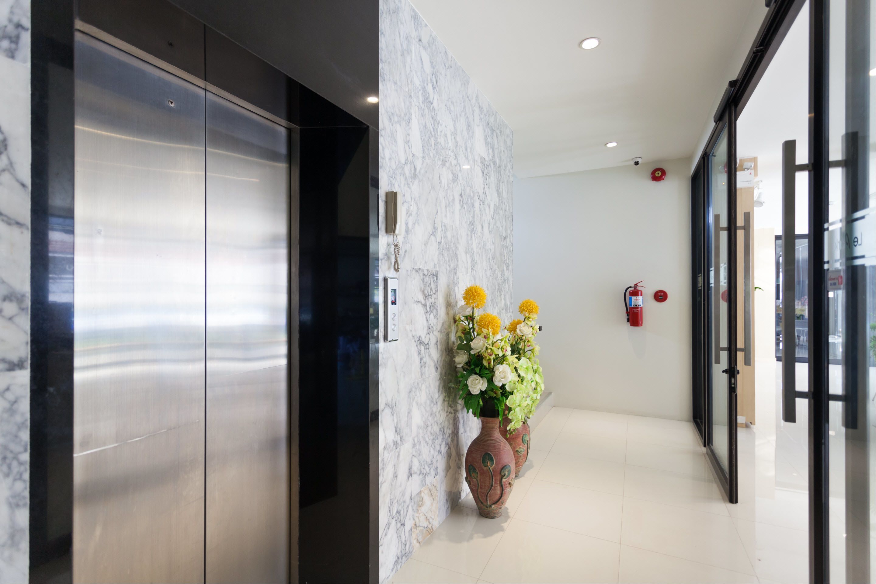 Een moderne lobby met marmeren wanden, een receptiebalie en twee vazen met bloemen.