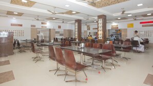 A spacious dining area with multiple tables and chairs, ceiling fans, and a visible wash area. - Hotel Sownthariyam (Palani)